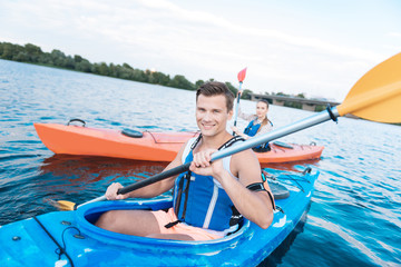 Obraz premium Summer date. Blonde-haired man smiling broadly while having nice summer date kayaking in the river