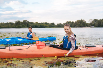 River flowers. Beaming blonde-haired woman looking at river flowers while kayaking with her husband