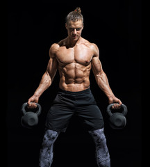 Fototapeta na wymiar Sporty young man working out with a kettlebells. Photo of muscular man with naked torso on black background. Strength and motivation