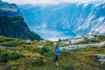 Naklejka na ściany i meble Happy sportive woman hiker before rain, relaxing and smiling in cliff during trip Norway. Trolltunga hiking route. Adventure, travel, leave your comfort zone concept.