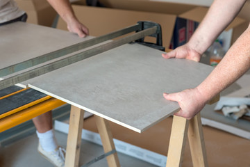 Workers cutting ceramic floor tiles tile with tile-cutter.
