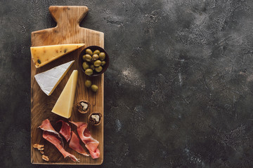 flat lay with assorted cheese, jamon and olives in bowl on dark surface