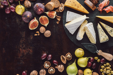 flat lay with assorted cheese, hazelnuts and fruits on dark surface