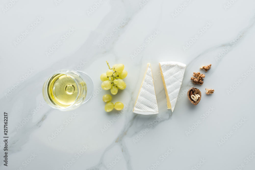 Wall mural flat lay with glass of wine, camembert cheese and hazelnuts on white marble surface