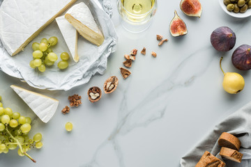 flat lay with cheese, wine and fruits arranged on white marble surface