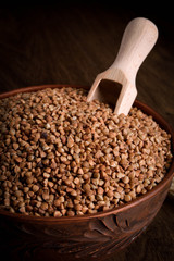 Buckwheat in a wooden bowl on a wooden background near the ears of wheat. wooden spoon with Buckwheat