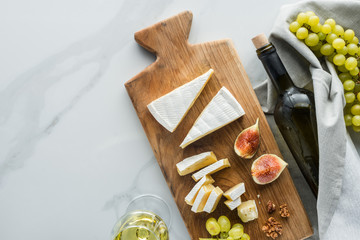 flat lay with food composition of camembert cheese on cutting board, wine and fruits on white...