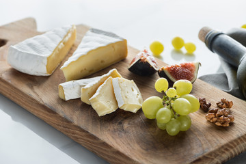 close up view of camembert cheese, grape and fig pieces on cutting board on white tabletop