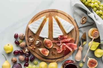 flat lay with cheese, jamon, figs, hazelnuts and grape on wooden board on white marble tabletop