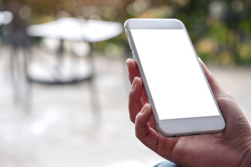 Mockup image of hands holding white mobile phone with blank desktop screen and blur background