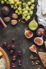 flat lay with arranged fruits, cheese and hazelnuts on dark surface