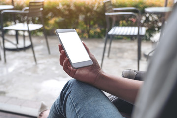Mockup image of woman's hands holding white mobile phone with blank desktop screen while sitting in cafe