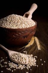 Pearl barley in a wooden bowl on a wooden background near the ears of wheat. wooden spoon with pearl barley