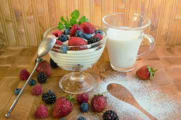 Milk dessert with strawberry raspberries raspberries blueberry blueberries and mint leaves in a glass vase on the table next to a cup of milk and a silver spoon