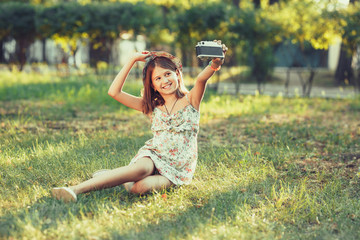 little girl is played by photo camera sitting on grass in park. Doing Selfie and photographing the...