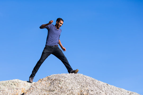 Young Man Taking Large Step Across  Boulders
