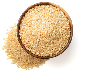 uncooked brown rice in the wooen bowl, isolated on the white background, top view