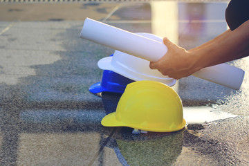 Businessman or engineer holding three helmets yellow, white and blue on concrete floor and water background, Safety and construction concept