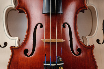 Closeup front side of completed violin,in front of half front side of raw violin,blurry light around