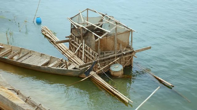 Old bamboo fish cage for rearing fish and wooden boat at water's edge ( close up )