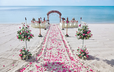 Beach wedding venue settings with decorating with bunch of red and pink roses petal on the aisle,...