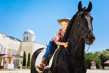 Obraz premium Cowboy girl. Cute cowboy girl wearing nice cowboy hat hugging her beautiful black horse