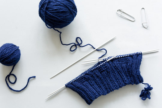 Girl knits blue hat knitting needles on gray wooden background. Process of knitting. Top view. Flat lay