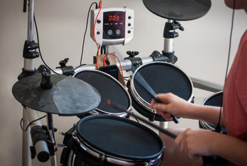 unrecognized boy in pink t-shirt practicing electronic drums with black drumsticks