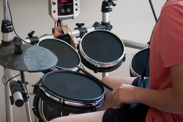 unrecognized boy in pink t-shirt practicing electronic drums with black drumsticks