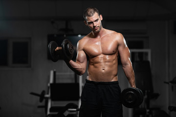 Plakat Man trains in the gym. Athletic man trains with dumbbells, pumping his biceps