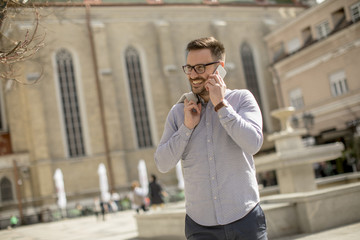 Cheerful young man uses mobile phone on street