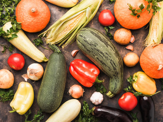 Assortment of fresh vegetables on dark old metal pan background. Courgettes, corn, pumpkin, zucchini, potato, pepper, onions, garlic