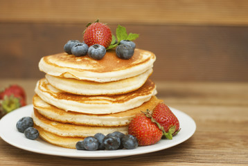 American pancakes served with strawberry and blueberry jam, delicious dessert for breakfast, rustic style, wooden background.