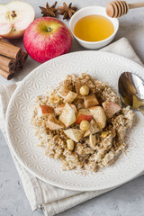 Oatmeal with fresh apples, nuts and cinnamon for Breakfast on the table, close-up, vertical