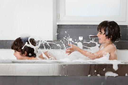Twin brothers fighting and splashing water in soapy bubble bath