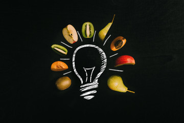 Colorful cut fruits surrounding a light bulb painted with chalk on blackboard as background - 217182012