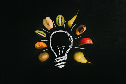 Colorful cut fruits surrounding a light bulb painted with chalk on blackboard as background