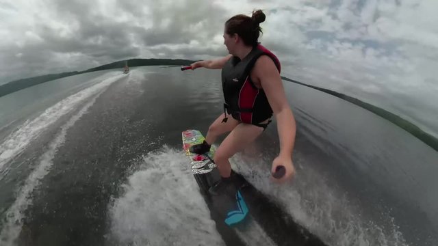 Extreme sports wakeboard athlete female ripping around a lake behind a boat