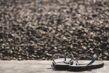 Old sandals Placed on a cement floor. The backdrop is a bokeh of pebbles that hit the sun in the morning.