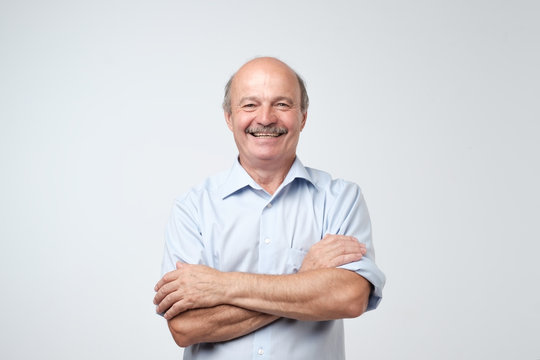 Charming Handsome Senior Man In Casual Blue Shirt Keeping Arms Crossed And Smiling