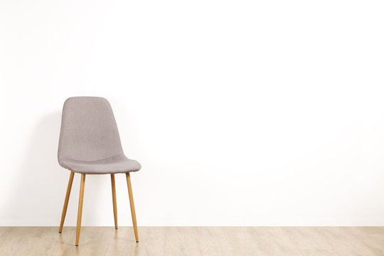 Single Elegant Gray Loft Style Chair Standing Alone On Wooden Floor In Empty Room, Big Blank Wall Background. Large Copy Space For Text. Only One Vacant Seat. Human Resources Hiring Campaign Concept.