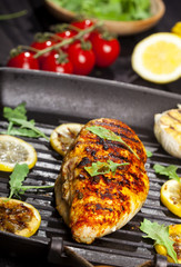 Grilled chicken fillet with spices and fresh vegetables in a pan on black background