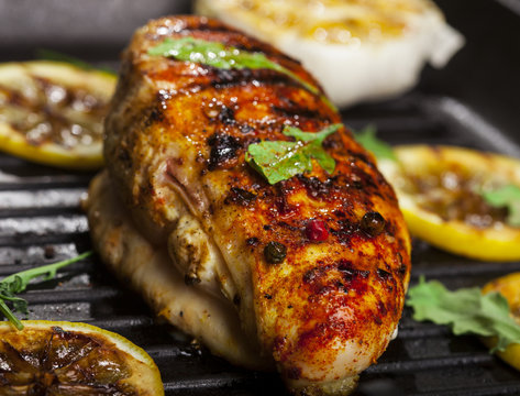 Grilled chicken fillet with spices and fresh vegetables in a pan on black background