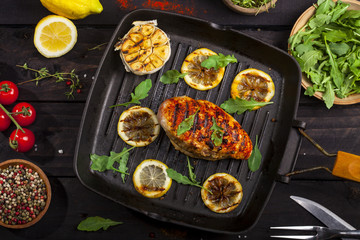 Grilled chicken fillet with spices and fresh vegetables in a pan on black background