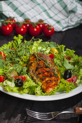 Grilled chicken fillet with fresh lettuce, thyme, cherry tomatoes, and olives in a plate on black background
