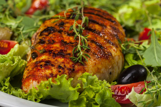 Grilled chicken fillet with fresh lettuce, thyme, cherry tomatoes, and olives in a plate on black background