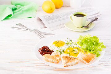 Scrambled eggs, fried bread, ketchup and lettuce leaves on a plate, cup of coffee and newspaper on the table. Ready-to-eat breakfast