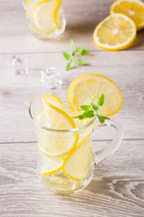 Refreshing cold mineral water with lemon, mint and ice cubes in glasses on a wooden table
