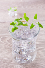 Cold mineral water with ice cubes and mint leaves in a transparent glass on a wooden table