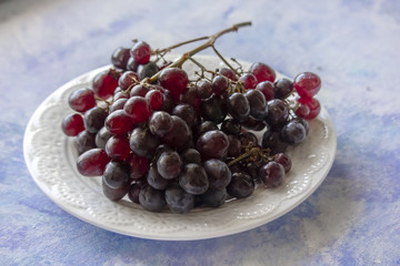 Black grapes in a white plate on the blue 